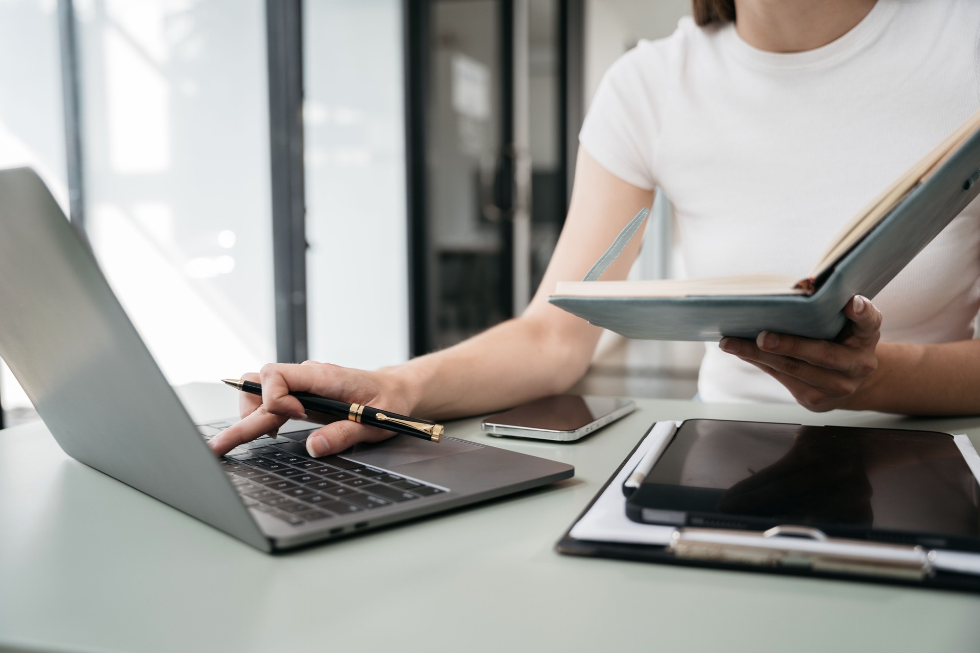 Female businessman use a smartphone and take notes in the notebook at the office desk in the morning.